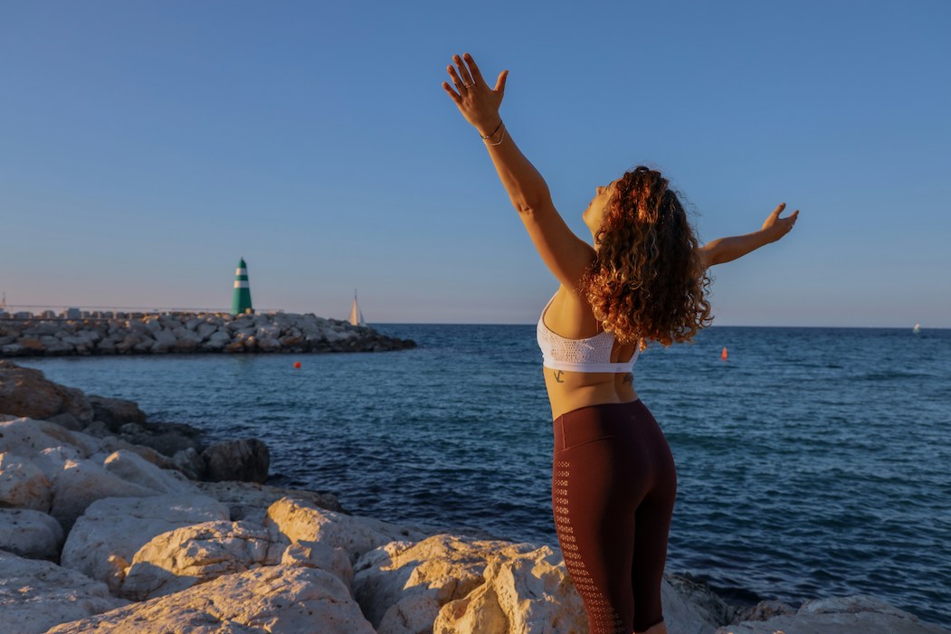 Woman on a rocky coastal beach with her arms out
