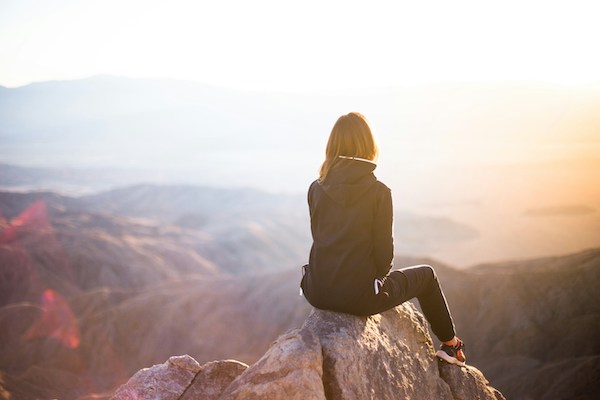 Woman sitting on the tip-top of a mountain looking out at the horizon